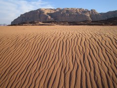 Sand und im Hintergrund Felsen in der Wüste in Jordanien