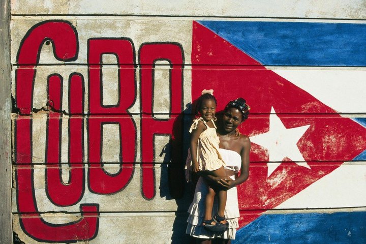 Kubanerin mit ihrem Kind auf dem Arm vor einer Kubafahne