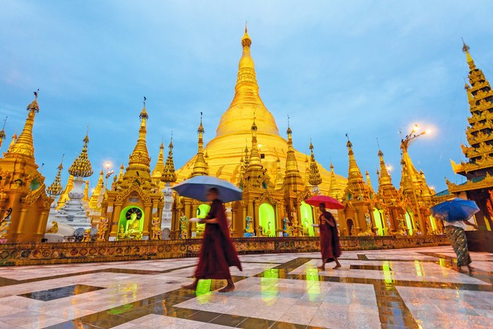 Einheimische mit Regenschirme gehen vor der Shwedagon Pagode