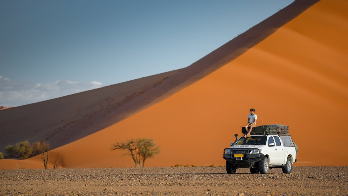 Mann sitzt auf seinem Camper vor einer grossen Sanddüne in Namibia