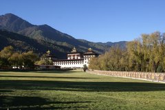 Blick über eine grüne Wiese zu einem Dzong in Bhutan