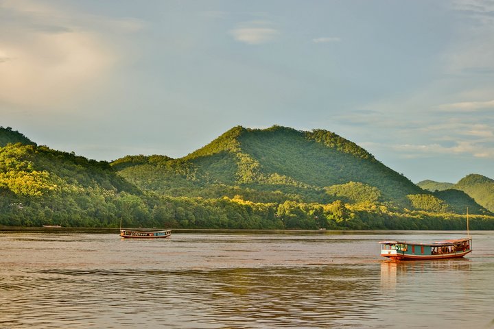 Ein Flussboot auf dem riesigen Mekong, dahinter Hügellandschaften