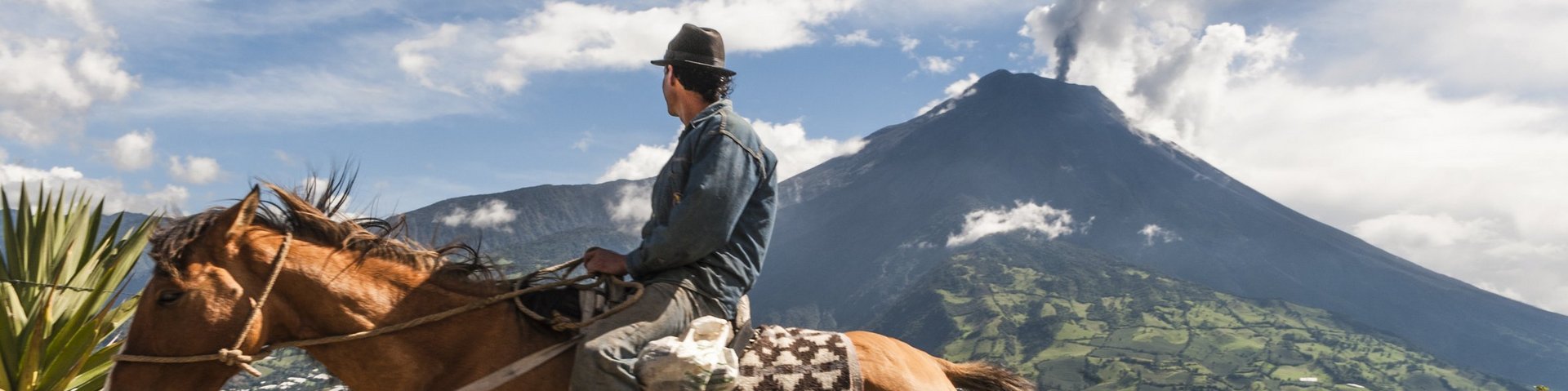 Einheimischer reitet auf seinem Pferd und im Hintergrund raucht es aus dem Vulkan Tungurahua
