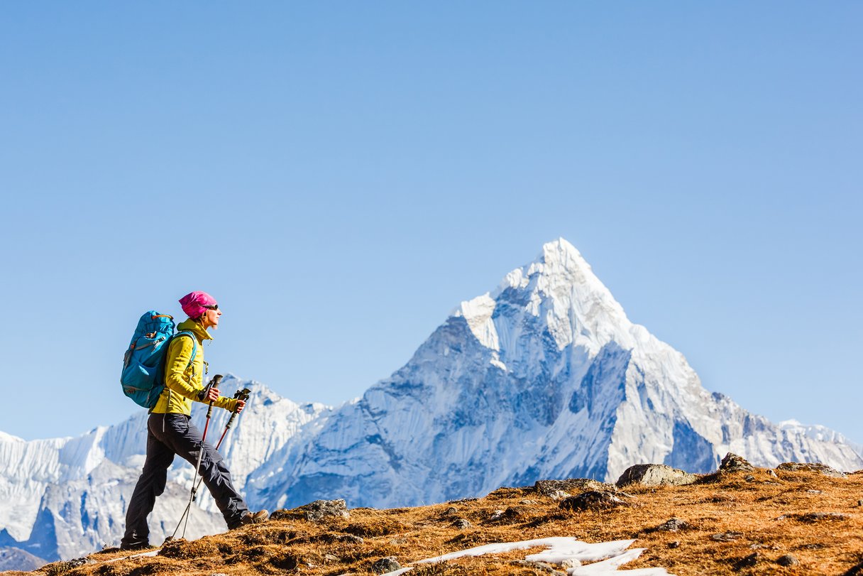 Frau wandert in Nepal, im Hintergrund ein mächtiger Berggipfel mit Schnee
