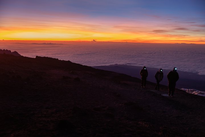 Drei Personen mit Stirnlampe steigen hoch zum Gipfel des Kilimanjaro