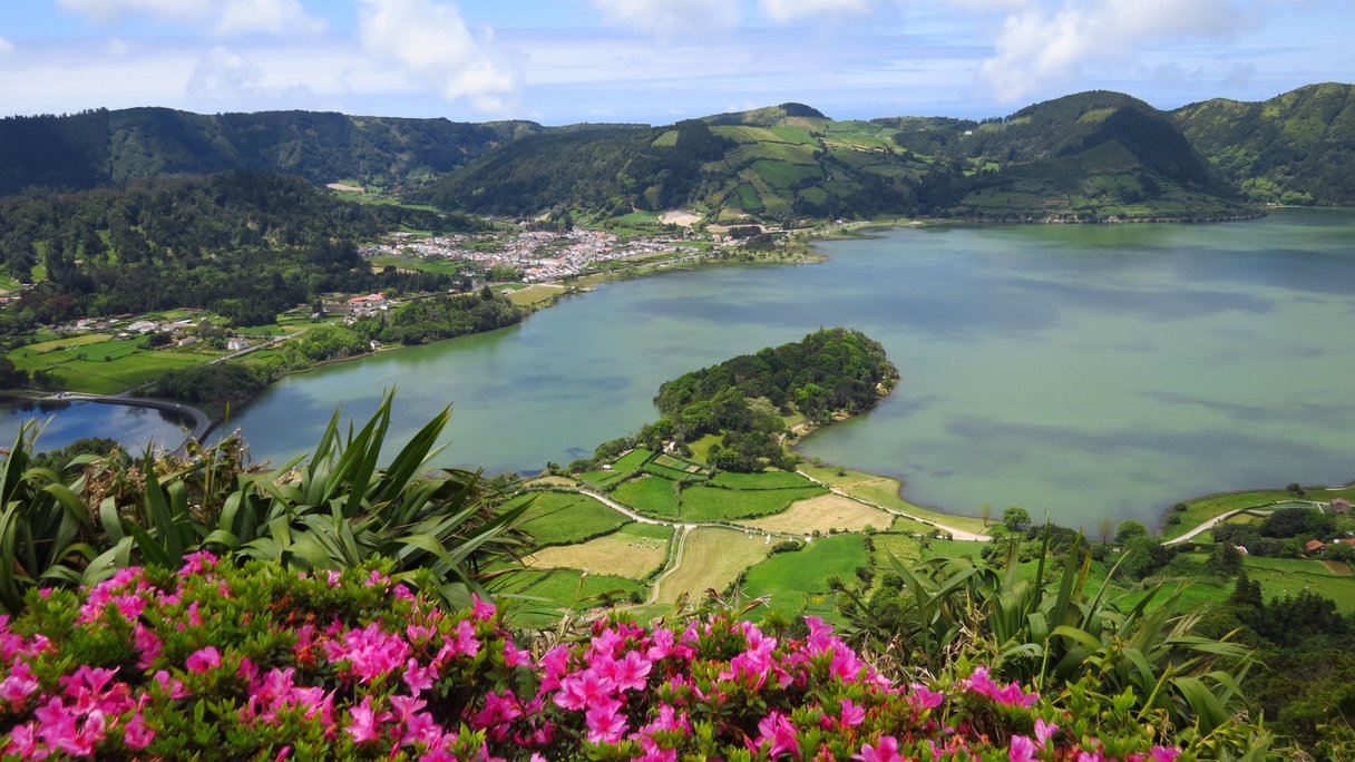 Blick über bunt blühende Blumen und einen See auf der Azoren-Insel São Miguel