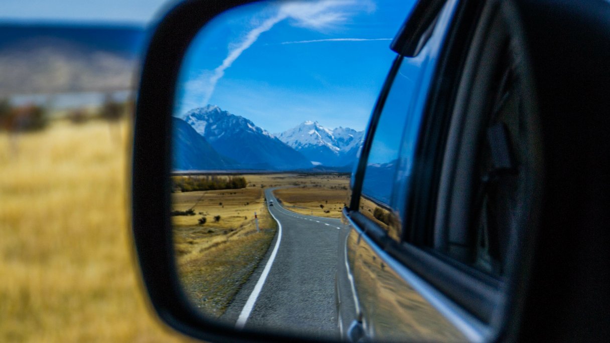 Blick durch den Rückspiegel auf die Strasse und die Berge von Neuseeland