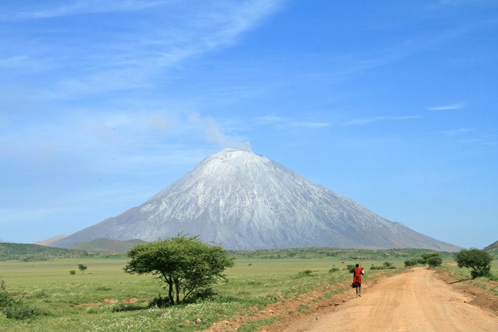 Masai geht auf einer Strasse, im Hintergrund der mächtige Kilimanjaro