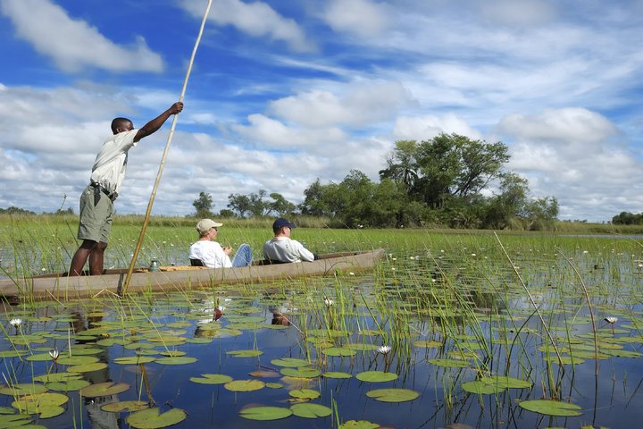 Zwei Touristen mit einem Guide auf einem traditionellen Mokoro-Boot in Botswana
