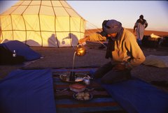 Ein Mann schenkt Tee ein in einem Wüstencamp in Marokko