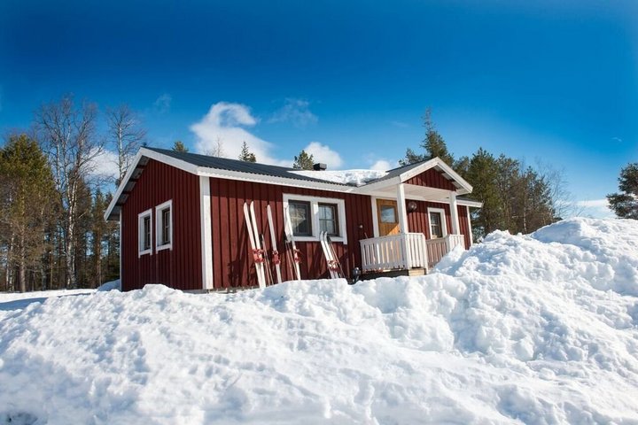 Rote Hütte im Camp von Rajamaa umgeben von Schnee und unter blauem Himmel