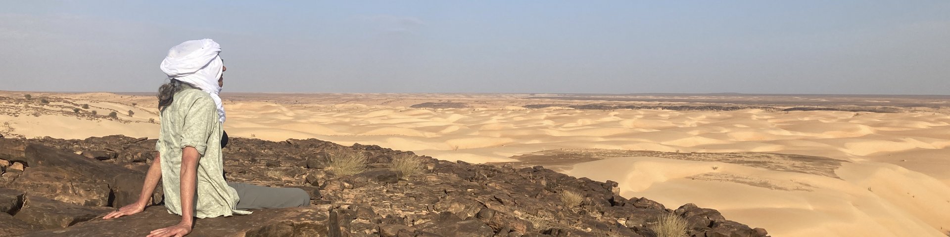 Reisende sitzend auf Felsen schaut auf Sanddünen