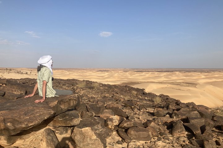 Reisende sitzend auf Felsen schaut auf Sanddünen