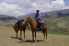 Ein Kirgise auf seinem Pferd mit einem weiteren Pferd unterwegs